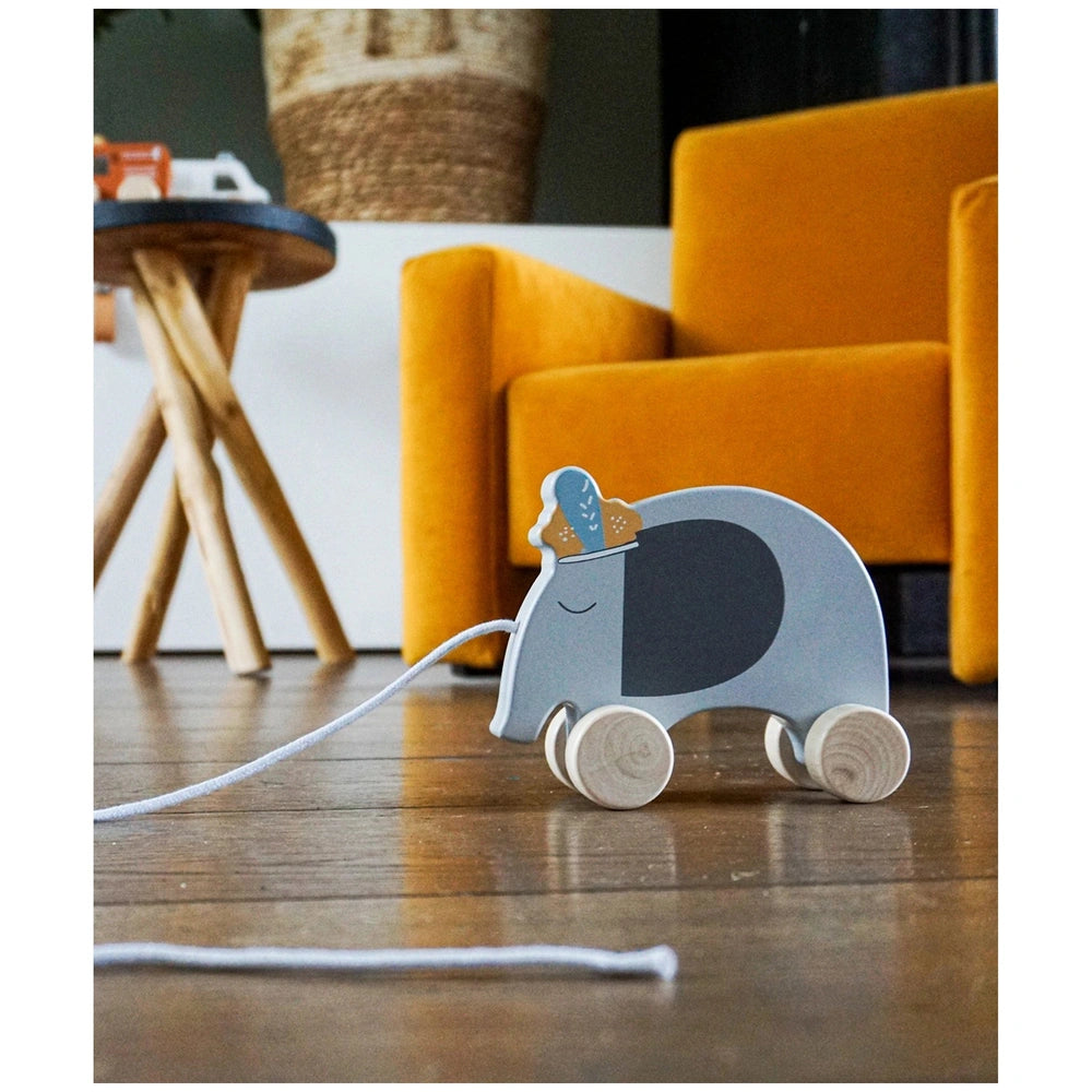 Gray wooden elephant pull along toy positioned on a wooden table in front of an orange fabric sofa against a white wall.